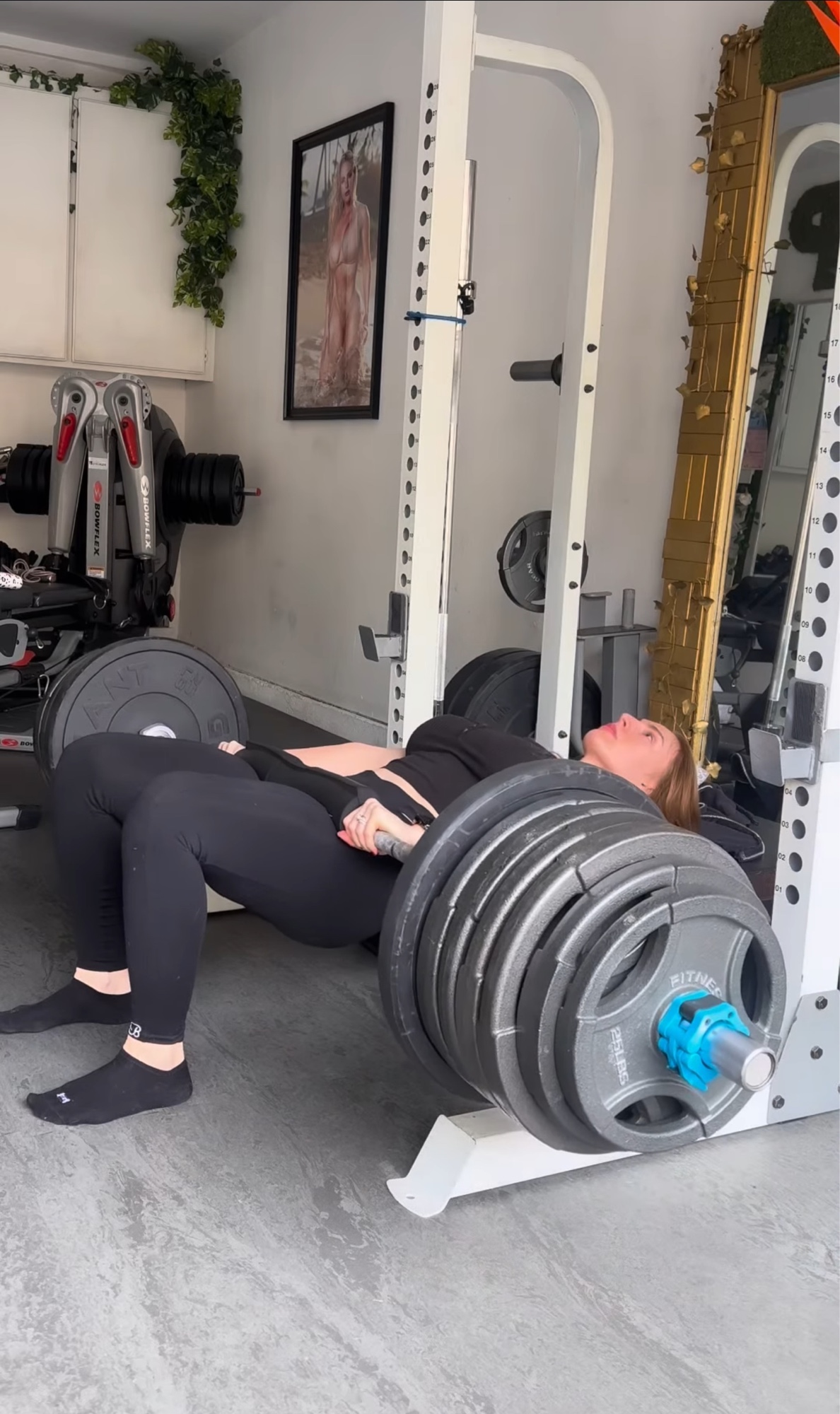 Amber Barbee training — hip thrust with a heavy loaded barbell in her home gym