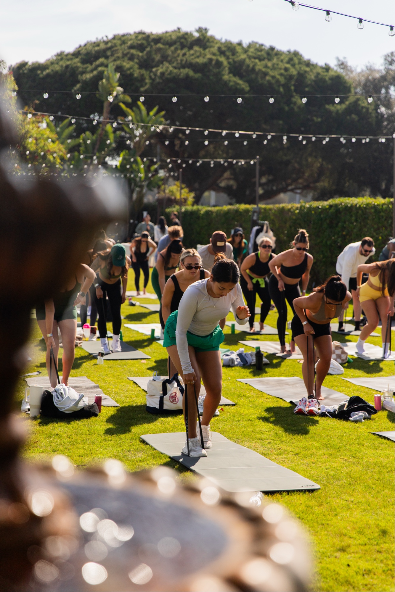 Club Sweat leading a large outdoor group Pilates class in San Diego with string lights and palm trees