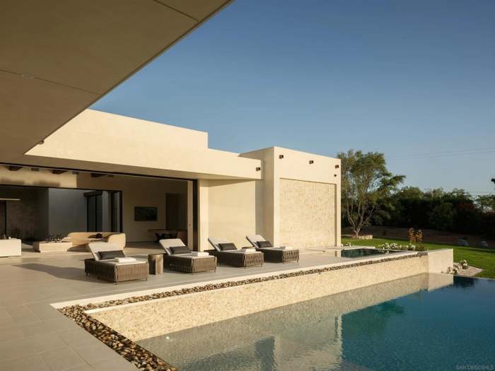 Infinity pool with travertine deck and lounge chairs overlooking olive groves