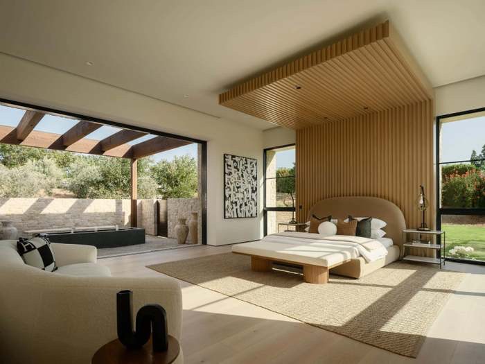 Primary bedroom with slatted wood canopy, jute rug, and pergola-shaded courtyard beyond