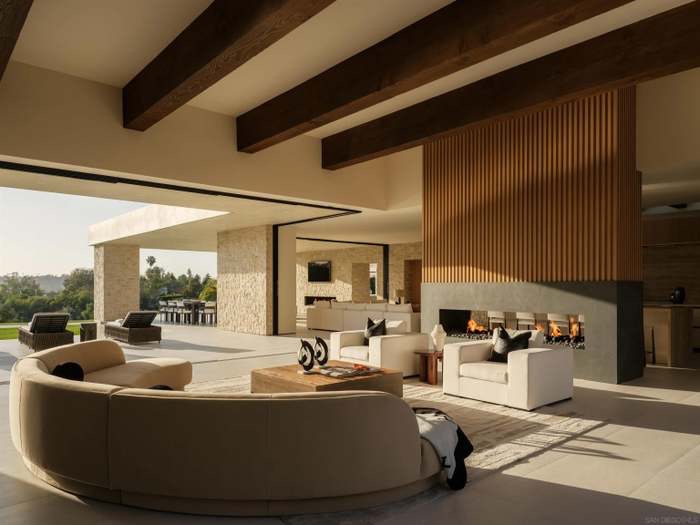 Great room with wood-beamed ceiling, curved sofa and open-air fireplace